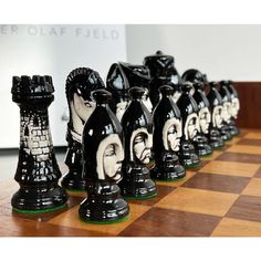 black and white chess pieces are lined up on a wooden board with the faces of people painted on them