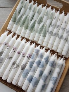 several white candles with blue and green leaves on them are lined up in a wooden tray