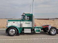 a green and white semi truck parked on the side of the road in front of a field