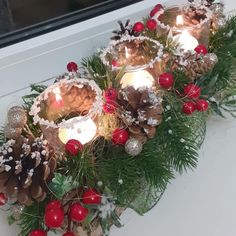 candles are lit in front of pine cones and holly wreaths on the window sill