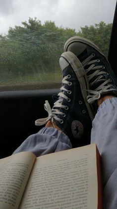 someone is sitting in the car with their feet on an open book and wearing converse shoes