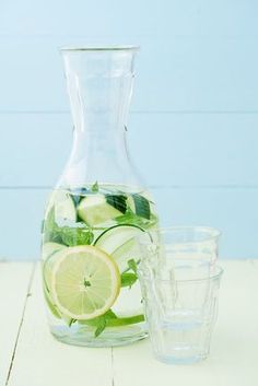 a pitcher filled with lemon slices and cucumbers next to two glasses on a table