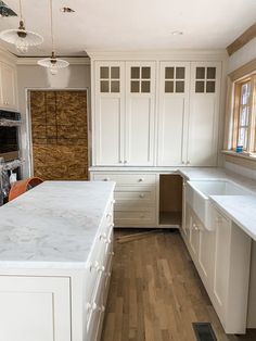 an empty kitchen with white cabinets and wood flooring on the walls, along with wooden floors