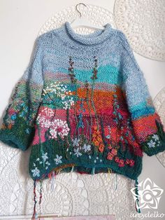 a sweater with flowers on it is hanging from a lace doily wall hanger