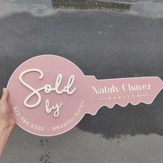 a pink sign that says sold by next to a person's hand holding it