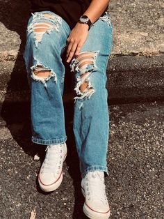 a person sitting on the ground wearing ripped jeans