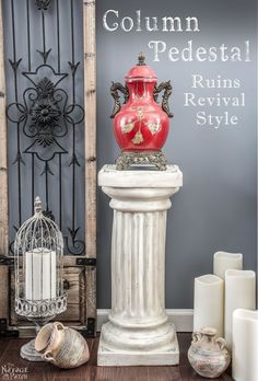 a red vase sitting on top of a white pedestal next to candles and other items