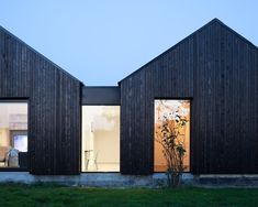 two wooden buildings with glass windows on each side and grass in the foreground at dusk