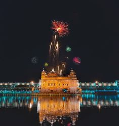 fireworks are lit up in the night sky above a building with water reflecting on it