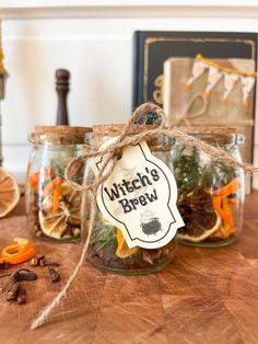 two glass jars filled with dried herbs on top of a wooden table next to an orange slice