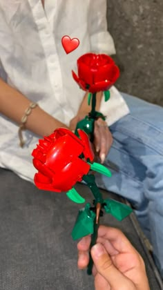 a person is holding two red roses in their hand and the other one has a heart on it