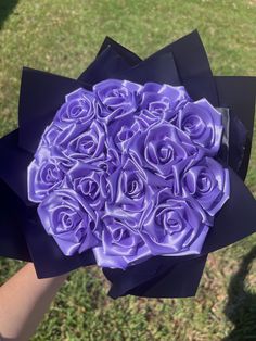 a bouquet of purple roses is being held by someone's hand in the grass