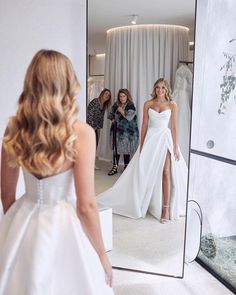 a woman standing in front of a mirror wearing a white dress and looking at her reflection