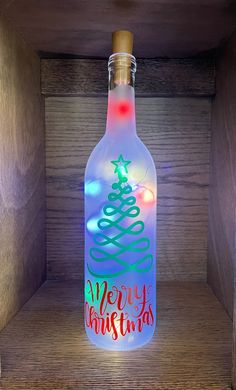 a lighted bottle with a merry christmas tree on it sitting in a wooden box next to a wall