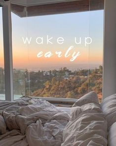 an unmade bed with the words wake up early in front of a large window