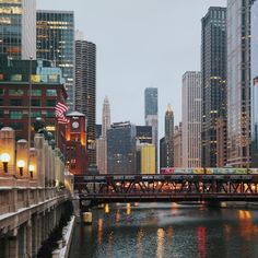 a train traveling over a bridge in the middle of a city with tall buildings on either side