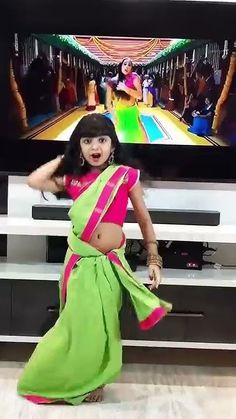 a woman in a green and pink sari standing in front of a flat screen tv