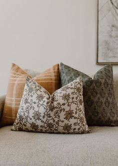 three pillows sitting on top of a couch in front of a framed painting and window