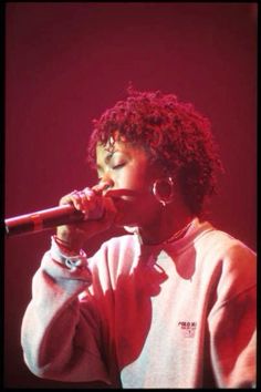 a woman singing into a microphone in front of a red background with her eyes closed