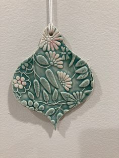 a ceramic ornament with flowers and leaves hanging from a hook on a wall