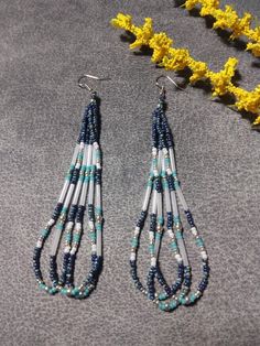 blue and white beaded earrings sitting on top of a table next to yellow flowers