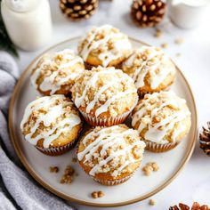 a white plate topped with muffins covered in frosting next to pine cones