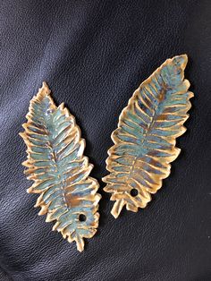 two gold and green leaf brooches on black leather