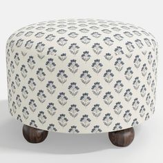 an upholstered foot stool with wooden legs and floral print on the top, in front of a white background