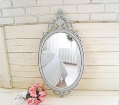 a mirror sitting on top of a white shelf next to a vase with pink flowers