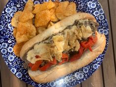 a blue and white plate topped with a hot dog covered in toppings next to potato chips