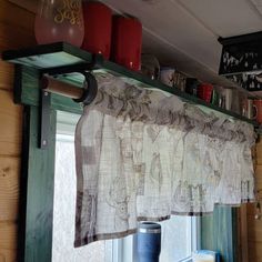 the kitchen window is covered with curtains and cups