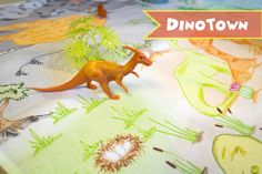 there is a toy dinosaur that is on the table cloth with other dinosaurs around it