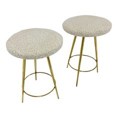 two round stools with gold legs and white upholstered fabric seat covers on them