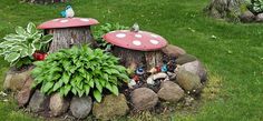 a garden with rocks, plants and gnomes in the grass next to a tree stump