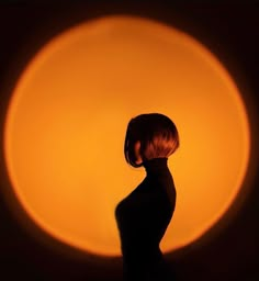 the silhouette of a woman in front of an orange circle with her hair pulled back