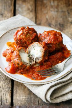 meatballs covered in marinara sauce on a white plate with a fork and napkin