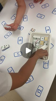 two children are playing with dominos on a white tablecloth that has blue letters and numbers