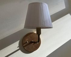 a wall light with a white shade on it's side and the lamp turned off