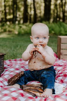 a baby sitting on top of a red and white checkered blanket holding food in his mouth