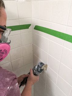 a woman in a pink shirt and goggles is painting a wall with green tape