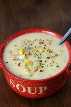 a red bowl filled with soup sitting on top of a wooden table next to a spoon