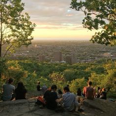 people are sitting on the edge of a cliff overlooking a cityscape at sunset