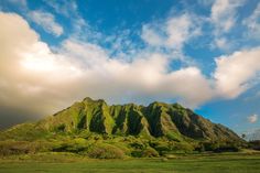 the mountains are covered in green grass under a cloudy blue sky