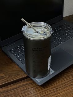 a laptop computer sitting on top of a wooden desk next to a cup with a straw in it