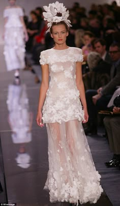 a model walks down the runway in a white dress with flowers on it's head