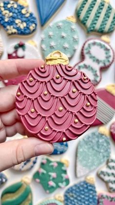 a hand is holding a pink ornament in front of cookies and other decorations