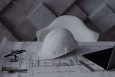 a white hard hat sitting on top of a blueprint next to a laptop computer