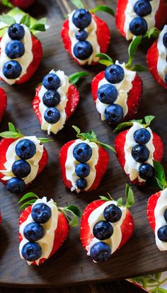 red, white and blue cupcakes are arranged on a wooden tray with strawberries