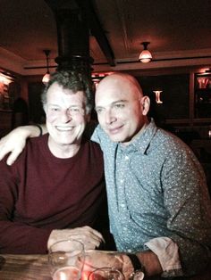 two men sitting next to each other at a table in a restaurant smiling for the camera