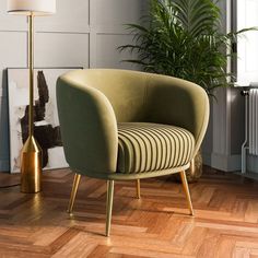 a green chair sitting on top of a wooden floor next to a lamp and potted plant